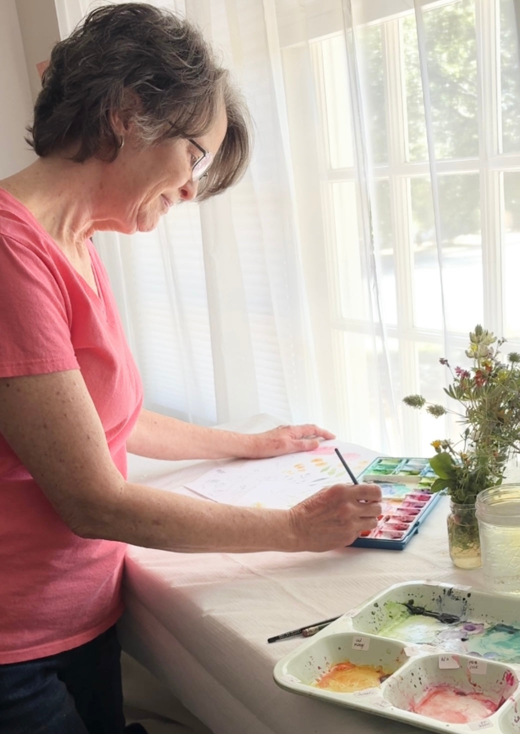 Woman painting with watercolors at a table by a window